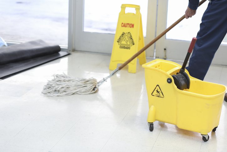 Unrecognizable man mopping floor in office building.